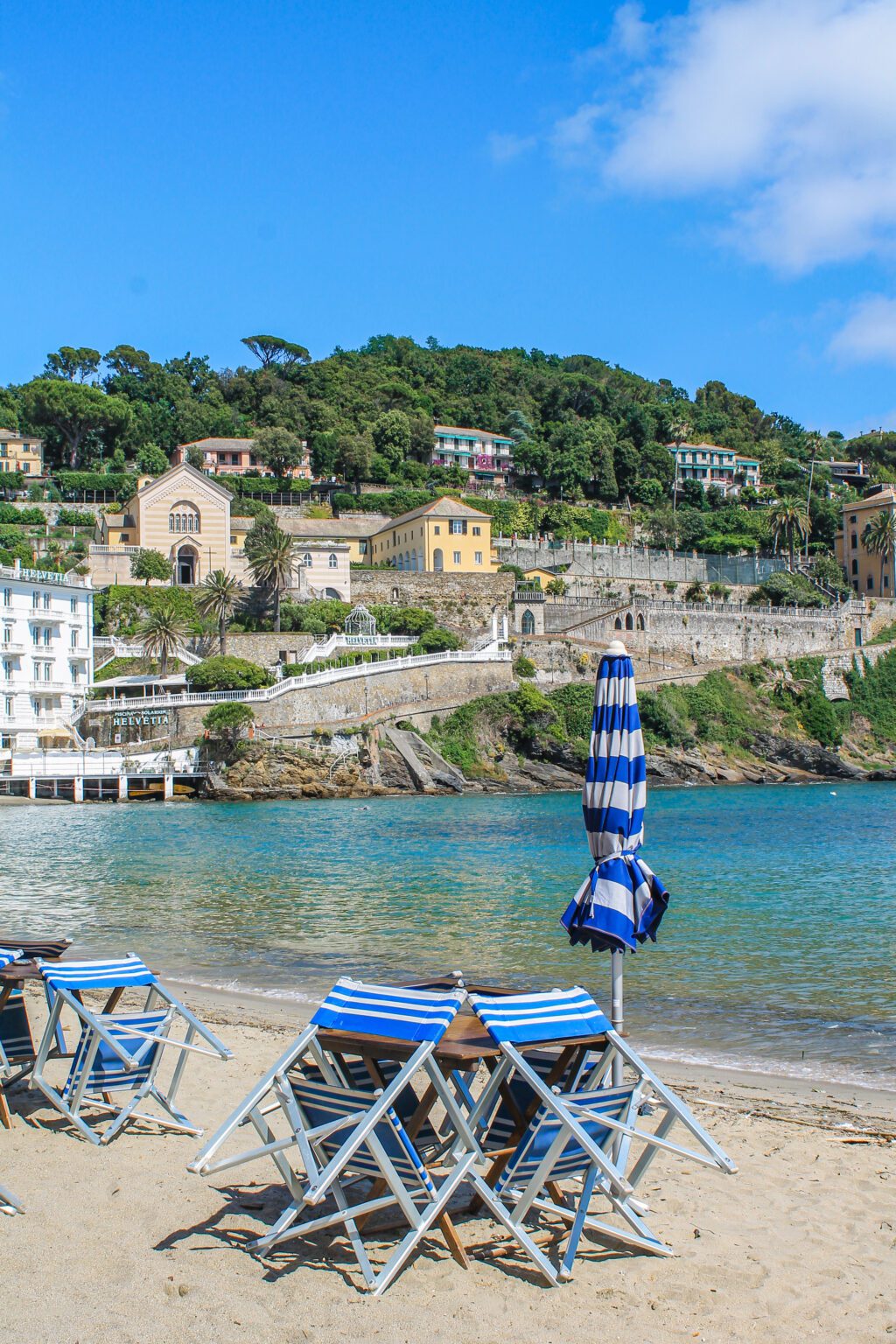 Ombrelloni e sedie blu, mare, costa con alberi e case sul mare