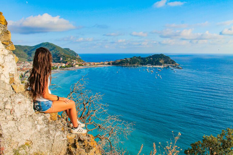 ragazza seduta su delle rocce con affaccio sul mare, cielo azzurro