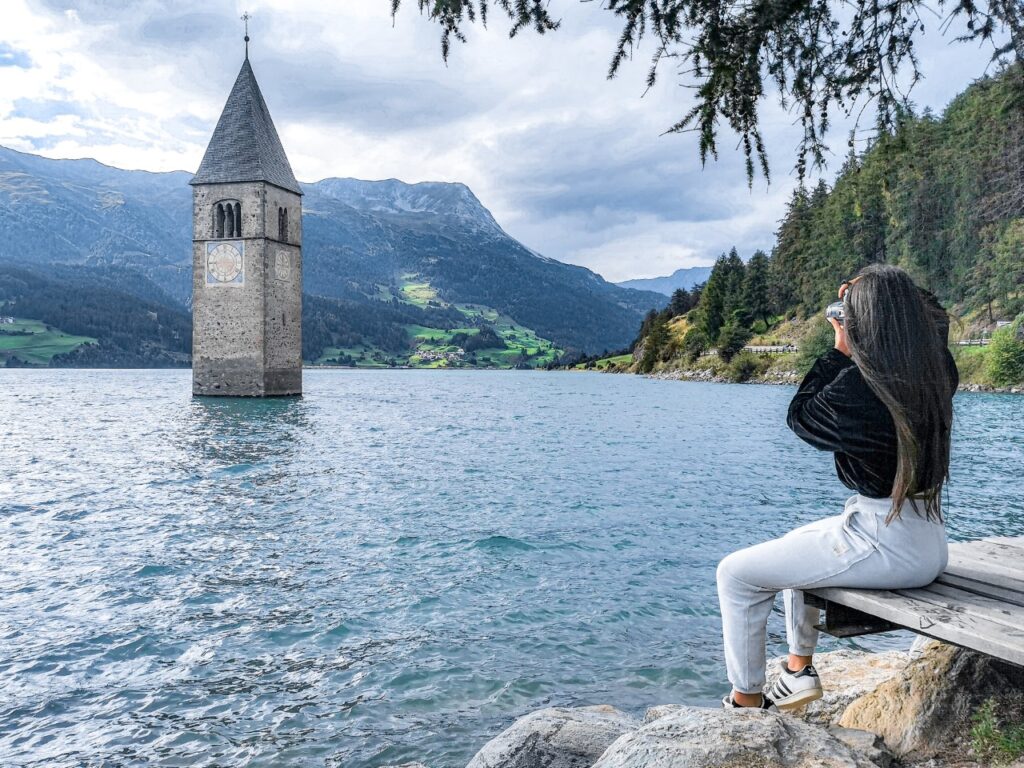 Ragazza seduta che fotografa, davanti al lago, campanile al centro del lago