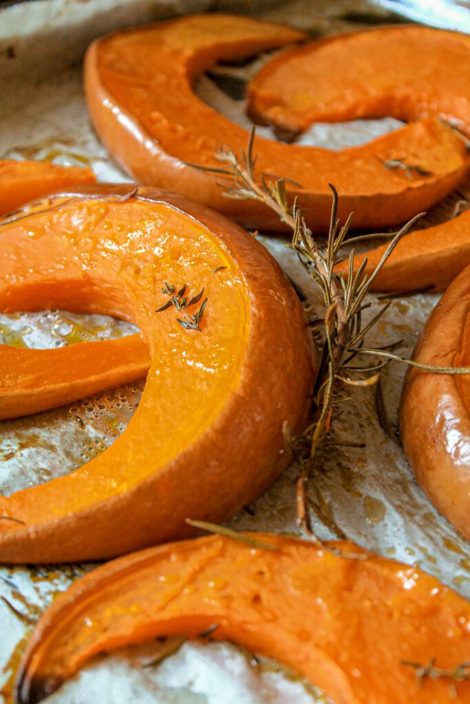 zucca al forno: fette di zucca su carta da forno, rametti di erbe aromatiche