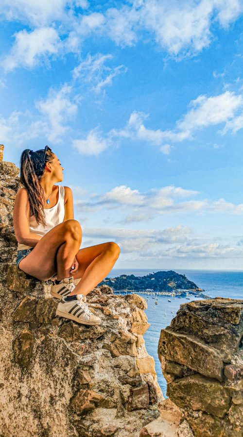 ragazza seduta su delle rocce con affaccio sul mare, cielo azzurro