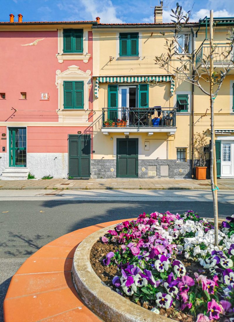 casa rosa e color panna, persiane verde scuro, aiuola con fiori colorati