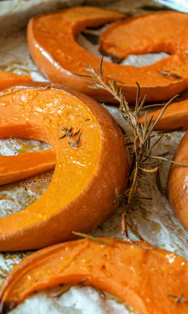 zucca al forno: fette di zucca su carta da forno, rametti di erbe aromatiche